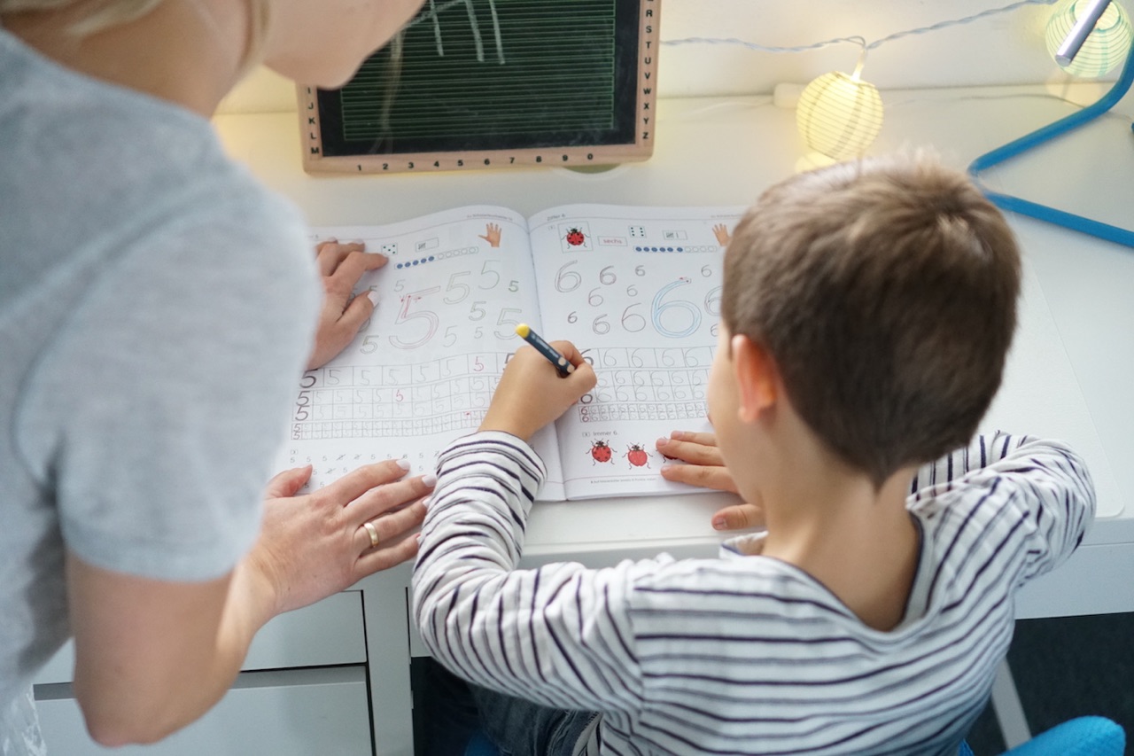 Mama stärkt dem Schulkind den Rücken beim Schulaufgaben machen.